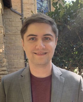 Dr. Ryan Hannagan smiling with short brown hair and wearing a grey blazer over a maroon shirt