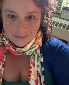 Bridget Lehane smiling with medium length curly brown hair and wearing a blue sweater and colorful scarf