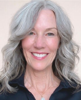 Dr. Christy Lyons Graham smiling with long gray wavy hair and wearing a navy blue button down collared top
