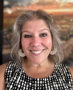 Heather Pacheco-Guffrey smiling with shoulder length gray hair and wearing a sleeveless black and white blouse