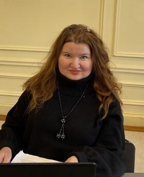 Dr. Alina Poklad smiling with long reddish brown hair and wearing a long sleeve black turtleneck sweater