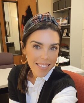 Dr. Ashley Rodrigues smiling with straight brown hair pulled back with a headband wearing a black knit vest over a white button-down blouse