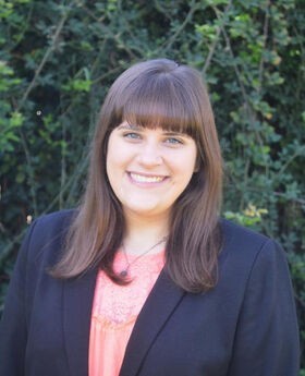 Dr. Brittany Russo smiling with long brown hair and wearing a navy blue blazer over a pink top