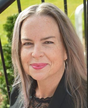 Ellen Scheible smiling with long straight gray hair and wearing a black blazer over a black top with lace in the neckline