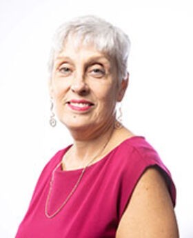 headshot of Elizabeth Souffront smiling with short gray hair wearing a sleeveless fuschia pink blouse and long earrings