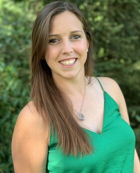 Meghan Stanton smiling with long straight brown hair and wearing a spaghetti strap green top with a v-neck