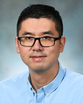 Dr. Eric Yao with short dark hair and wearing black rim glasses and a blue button down shirt