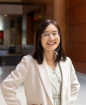 Dr. Hui Zhang smiling with medium length dark brown hair and wearing silver rimmed glasses and an off white blazer over a white top