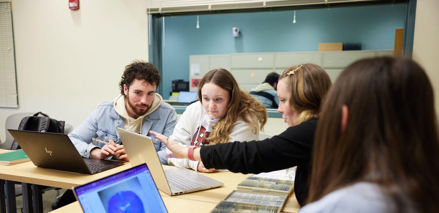 four students sitting at a table reviewing and discussing rat brain scans on their laptops