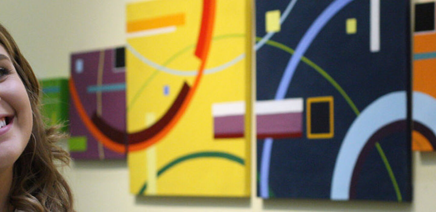 BSU student artist smiles in front of her artwork displayed on exhibit