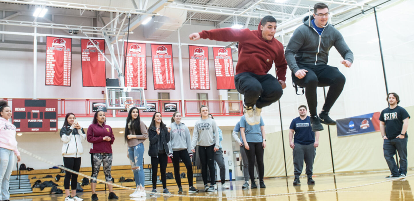 a physical education class in the BSU Tinsley Center gym with 2 male students jumping a long rope while the rest of the class watches