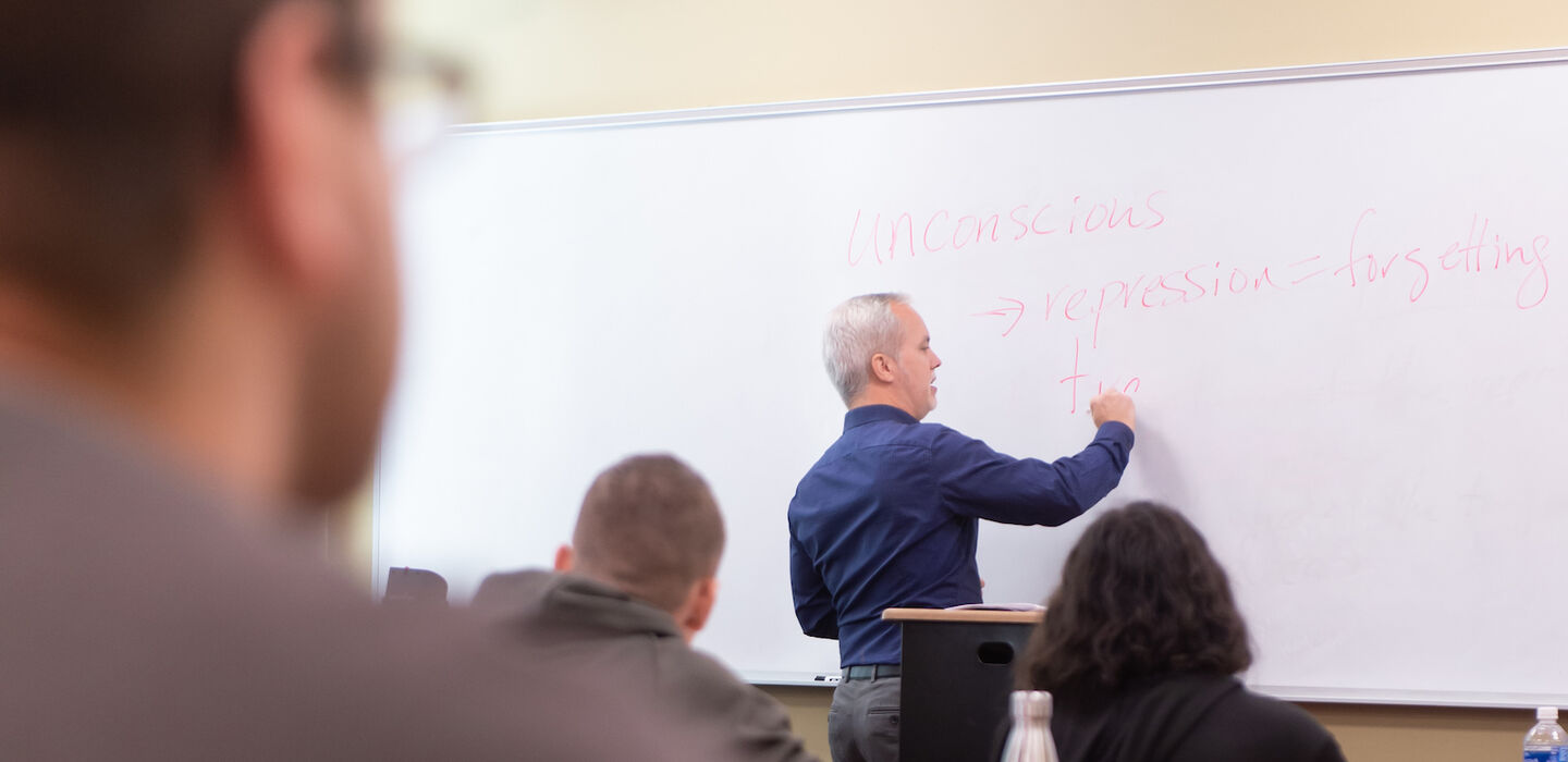 Dr. Matt Bell writing on the white board at the front of a classroom as students look on