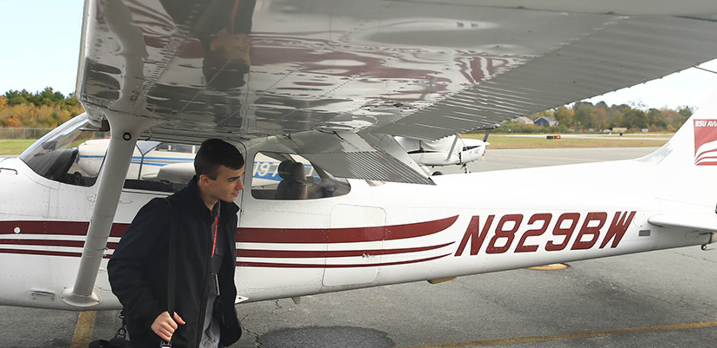 BSU aviation student walking under the wing of a parked BSU aviation plane