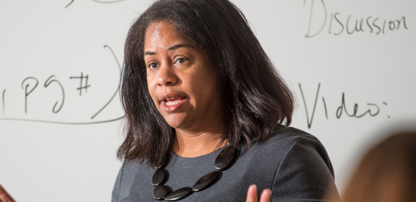 Dr. Mia Ortiz teaching a class in front of a white board with notes about class on it