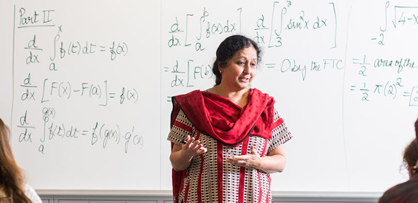 Dr. Uma Shama teaching a calculus class standing in front of a white board covered with equations with students looking on
