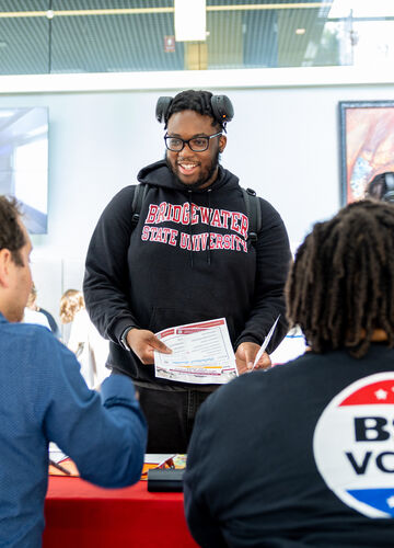 a BSU student smiles while picking up materials and interacting with a person at a BSU Votes table 