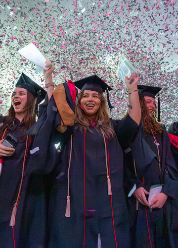graduating students celebrate at Commencement as confetti fills the sky above them