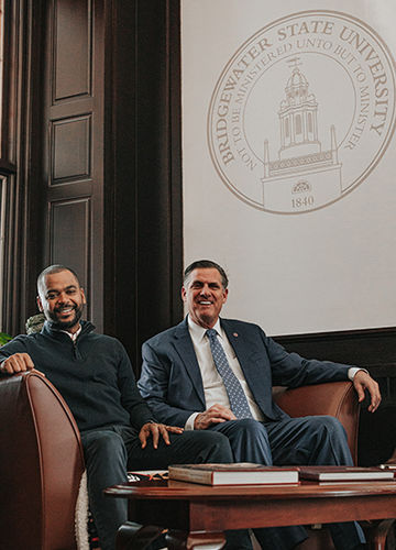 Harold Tavares and President Fred Clark sit in front of a banner with a BSU seal.